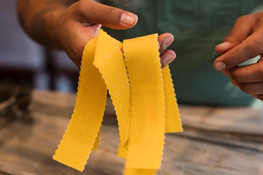 Yellow pasta strands held by hands against a blurred background