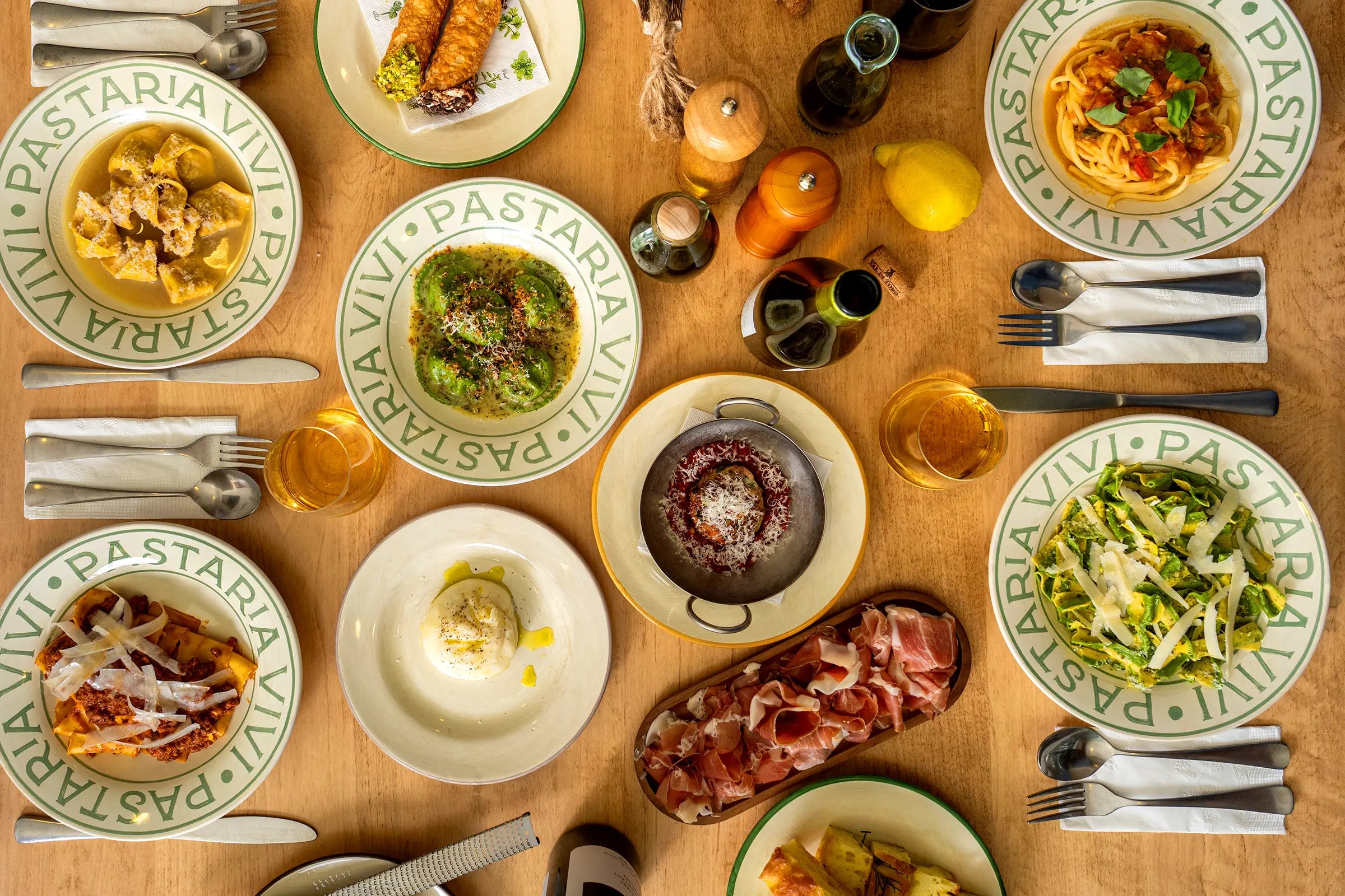 Diverse pasta dishes on plates with various sauces and ingredients on a wooden table.