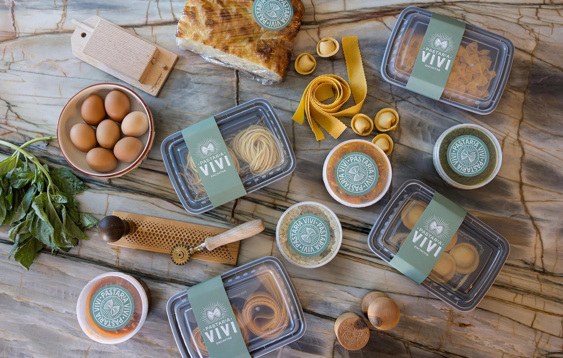 Assorted food items including eggs, pasta, and bread on a wooden surface with Pastaria Vivi branding.